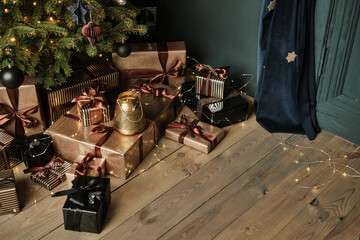 Close-up black and gold gift boxes under a Christmas tree on a wooden floor. Stylish packaging