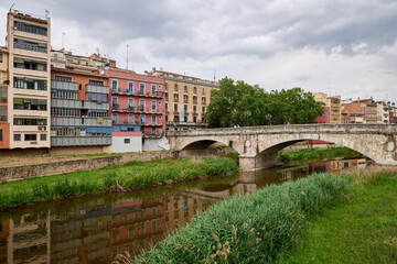 Colorful yellow and orange houses and bridge Pont de Sant Agusti reflected in water river Onyar, in Girona, Catalonia, Spain. Church of Sant Feliu and Saint Mary Cathedral at background. BRIDGE in the