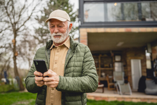 One senior man stand in front of tiny house in day use smart phone