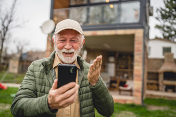 One senior man stand in front of tiny house in day use smart phone