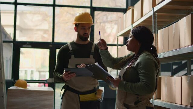 Logistics coordinators in warehouse inputing updated products info on online shopping website, walking through retail workspace aisles analyzing labels on wares, crosschecking with inventory list