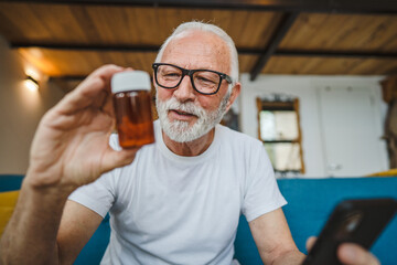 senior man sit at home hold bottle medicine pills drugs and smartphone