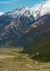 Cars driving along a winding road at the base of snow capped mountains in New Zealand