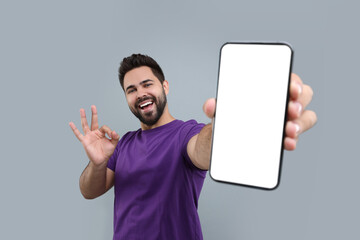 Young man showing smartphone in hand and OK gesture on light grey background