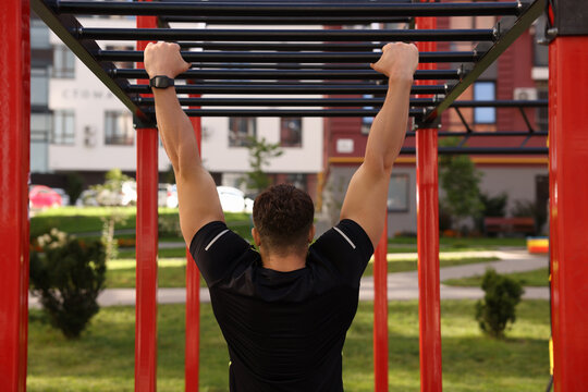 Man training on monkey bars at outdoor gym, back view