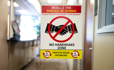 Sign stating No Handshake Zone in an office. The sign refers to reducing spreading germs. Covid Related sign