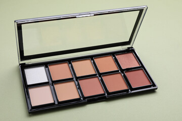 Colorful contouring palette on pale green background, closeup. Professional cosmetic product