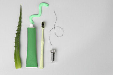 Tube of toothpaste, toothbrush, dental floss and fresh aloe on light grey background, flat lay....
