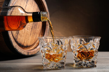 Pouring whiskey into glass from bottle near wooden barrel on table