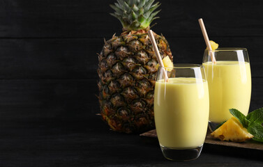 Tasty pineapple smoothie and fruit on black table. Space for text