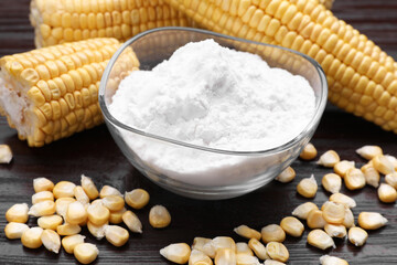Bowl with corn starch, ripe cobs and kernels on dark wooden table, closeup