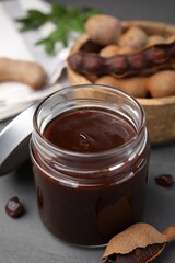 Jar of tasty tamarind sauce and fresh pods on grey wooden table