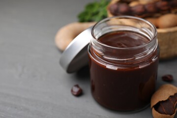 Jar of tasty tamarind sauce and fresh pods on grey wooden table. Space for text