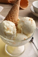 Delicious scoops of vanilla ice cream with wafer cone in glass dessert bowl on table, closeup