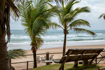 Fachada de resort com coqueiros, palmeiras e redes na sombra, no litoral do nordeste brasileiro durante uma tarde de verão.