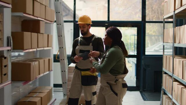 Chief logistics officer and employee preparing warehouse orders for delivery, using tablet to verify shipping informations, receiving phone call while scanning parcels labels in repository
