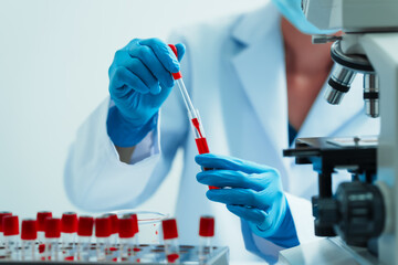 Close up dedicated hematology lab technician scrutinizing blood sample analysis under microscope, scientific laboratory research and drug testing concept, red color liquid