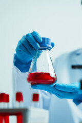 Close up dedicated hematology lab technician scrutinizing blood sample analysis under microscope, scientific laboratory research and drug testing concept, red color liquid