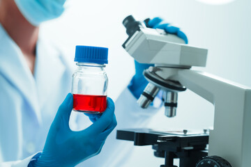 Close up dedicated hematology lab technician scrutinizing blood sample analysis under microscope, scientific laboratory research and drug testing concept, red color liquid