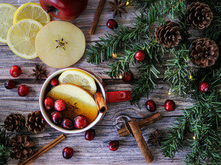 Christmas background flat lay with hot tea infused with fresh apple, lemon, cinnamon and cranberries on a textured wooden surface and green garland for Christmas spirit.