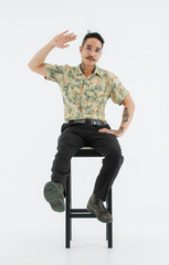 Naklejka premium Isolated cutout studio full body shot Asian vintage classic male fashion model with mustache neck arm tattoo wearing eyeglasses in casual outfit posing sitting on chair on white background