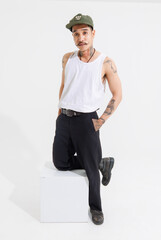 Isolated cutout studio shot Asian vintage classy mustache with neck arms hands tattoos male fashion model in casual fashionable sleeveless shirt cap boots posing standing on white background.
