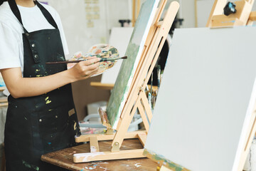 Young Asian female artist painting on canvas doing art projects on her studio.
