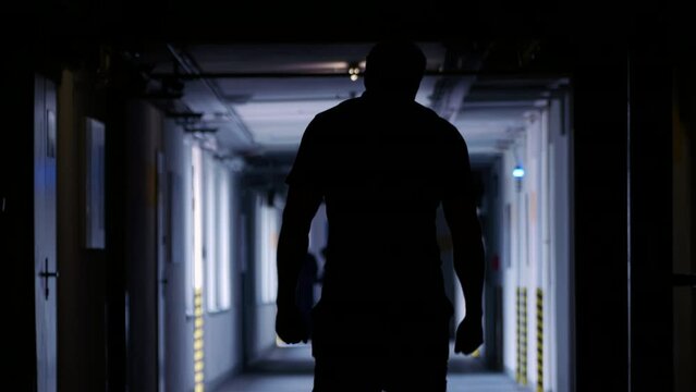 Factory worker in the workshop of an industrial plant: rear view of an unknown person in the dark, walking through the black hall. Image of an unknown worker. Human shadow. Slow motion