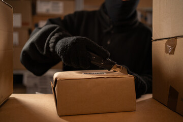 Stealing parcels and damaging the packaging of goods in the warehouse or post office. Man in balaclava and gloves in storehouse. Stealing and problems with the safety of cargo.