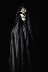 Fototapeta na wymiar A chilling portrait of a demon with a skull face draped in a black gown, looming ominously against a pitch-dark backdrop, encapsulating the essence of Halloween