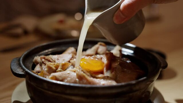 Steaming stock sauce cascades gracefully onto a meat bowl crowned with a perfectly poached egg. The golden yolk glistens, creating a mouthwatering spectacle of flavors. High quality 4k footage