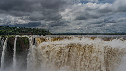 The famous impressive Devil's Throat Waterfall. Powerful streams of foaming water collapse into the abyss. Spray and fog. Clouds in the sky. Iguazu Falls. Argentina.