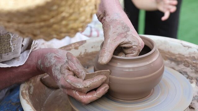 The potter's hands formed clay pot on a potter's wheel. The master potter works in a workshop