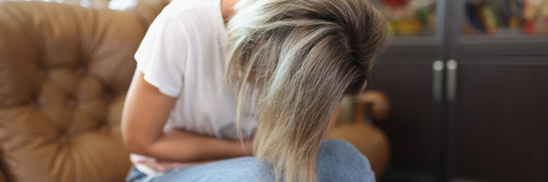 Female sitting on sofa, touching belly and writhing in pain