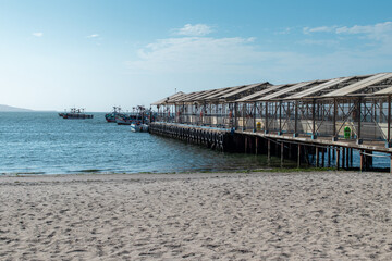 Fototapeta na wymiar Muelle en la Mar con botes y personas a la orilla de la playa