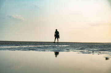 Fototapeta na wymiar calm man walking in the sand. Man goes to the sea on dark sand beach under sunset sky.