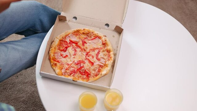 Top view of round white table with delicious pizza and two glasses of fresh orange juices indoors. Crop of adult wearing blue jeans making picture on smartphone. Fast food lunch.