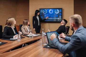 Business meeting in the conference room. A businesswoman is talking to her colleagues while an animated chart data is displayed on the computer screen.