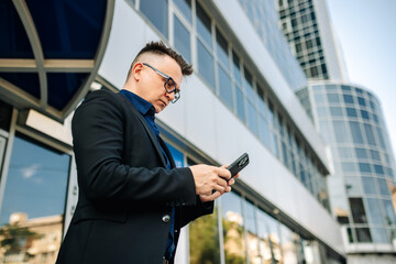 Closeup happy handsome male businessman successful on the city street. Portrait of a successful man outdoors. Modern gadgets for lifestyle.