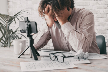 One man desperate holding head with hands in front of a desk full of business documents and phone...