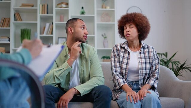 Frustrated african american couple having therapy session with family psychologist during marital crisis. Young husband and wife in casual attire talking emotionally while sitting together on couch.