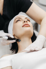 Obraz na płótnie Canvas Cosmetology clinic. Professional female cosmetologist doing hydrafacial procedure while being a work. Attractive nice woman lying on the medical bed while having beauty procedures
