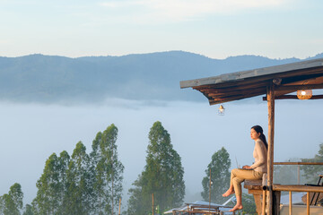 Fototapeta na wymiar Asian woman working using laptop computer on wooden balcony Tourist enjoying morning mist on hill and working using laptop at sunrise and morning light on mountain top with sea of mist in Thailand