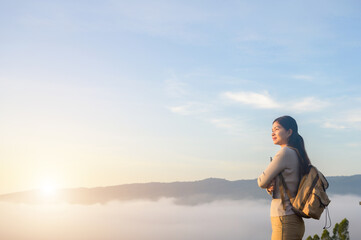 Asian female tourist or traveler Relaxing enjoying the morning mist at sunrise and morning light on a winter mountain peak in Thailand.