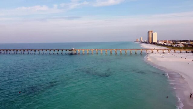 Aerial shot of the silhouette of a fishing pier on the ocean with a colorful and golden sunrise. Aerial of Panama City Beach Pier at Pier Park over the gulf of mexico turquoise blue and green water