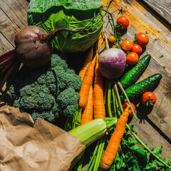 Colorful vegetables in a brown paper shopping bag on a wooden table. Different vegetables on the table made of dark wood. Raw vegetables from the store. Products in a paper eco-bag. Selective focus.