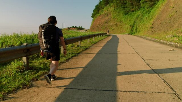 young woman hiker with a backpack walks confidently up a steep road on her hike