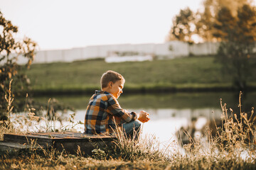 Kid boy sitting near a river, pond or lake and smiling. Autumn season. Happy childhood.