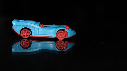 Side shot of a toy plastic race from new generation or racing car on black background on a reflective surface with selective focus - obrazy, fototapety, plakaty