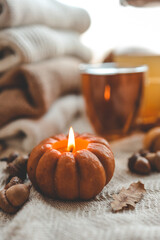 Burning candle in the shape of a pumpkin and a cup of tea, autumn mood